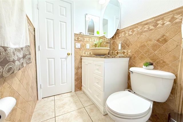 bathroom featuring tile patterned flooring, vanity, wainscoting, toilet, and tile walls