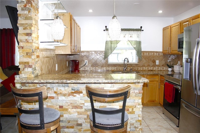 kitchen with a peninsula, light tile patterned flooring, light stone countertops, a sink, and appliances with stainless steel finishes