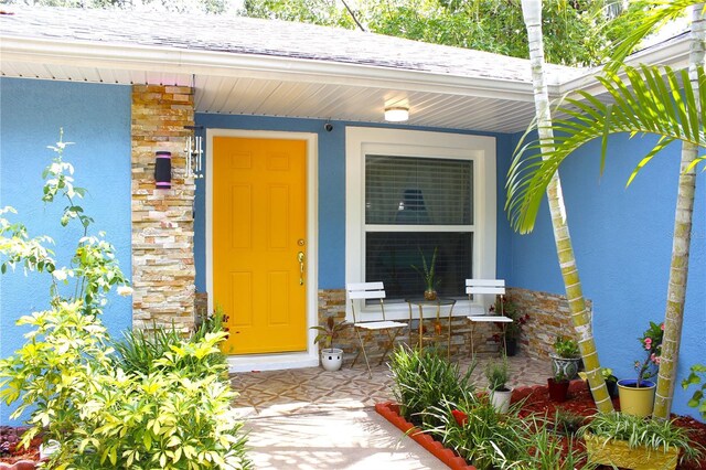 3306 E Chelsea St, Tampa, FL 33610 - property entrance with a porch, roof with shingles, stucco siding, and stone siding