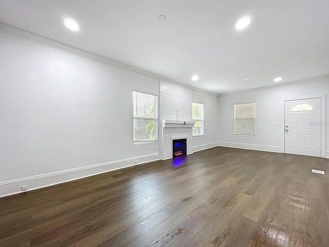 unfurnished living room featuring dark wood-style flooring, a glass covered fireplace, crown molding, and baseboards