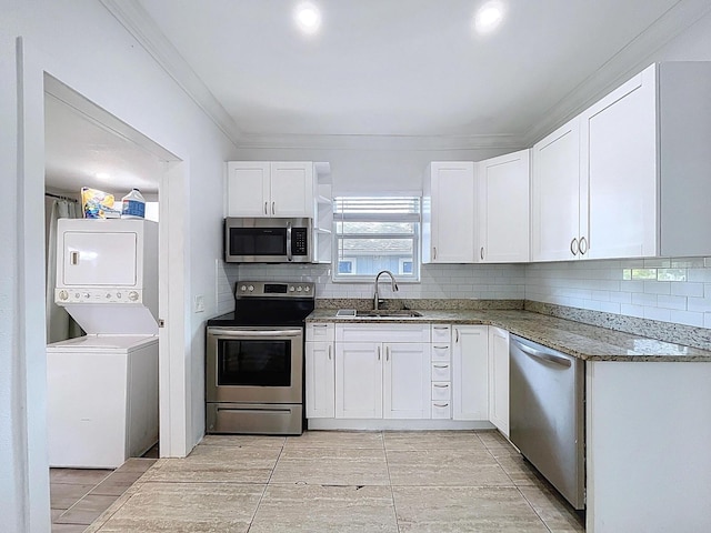 kitchen featuring a sink, stacked washing maching and dryer, stainless steel appliances, dark stone countertops, and white cabinets