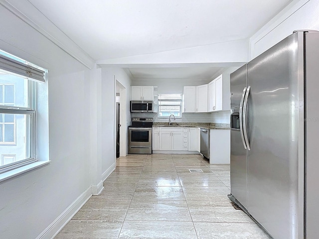 kitchen featuring white cabinetry, a sink, appliances with stainless steel finishes, dark countertops, and baseboards