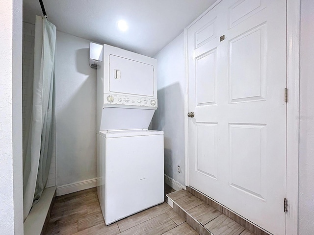 laundry area with light wood-style floors, stacked washing maching and dryer, laundry area, and baseboards