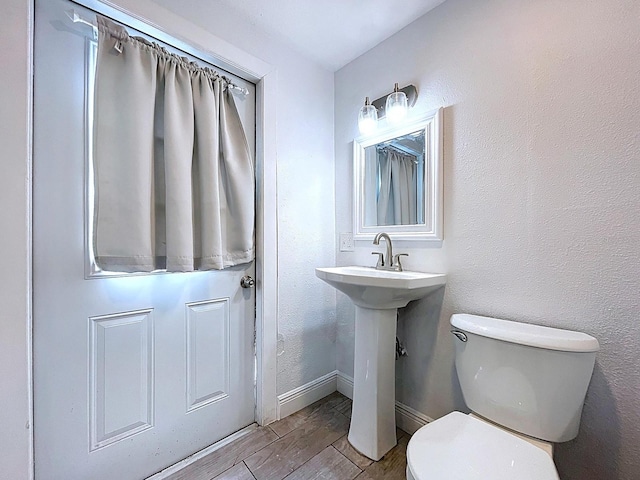 bathroom with toilet, wood finish floors, baseboards, and a sink