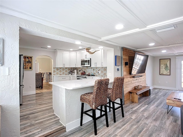 4231 8th St N, Saint Petersburg, FL 33703 - kitchen with a peninsula, light wood-type flooring, arched walkways, light countertops, and appliances with stainless steel finishes