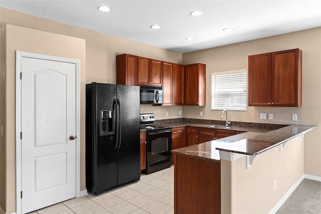 kitchen featuring brown cabinets, a sink, dark stone countertops, a peninsula, and black appliances