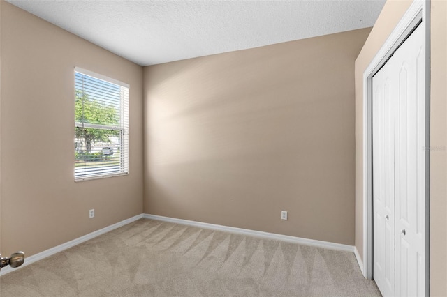 unfurnished bedroom featuring baseboards, light carpet, a closet, and a textured ceiling