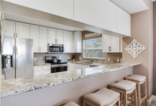 425 150th Ave Unit 2301, Madeira Beach, FL 33708 - kitchen with stainless steel appliances, light stone counters, a peninsula, white cabinets, and a kitchen bar