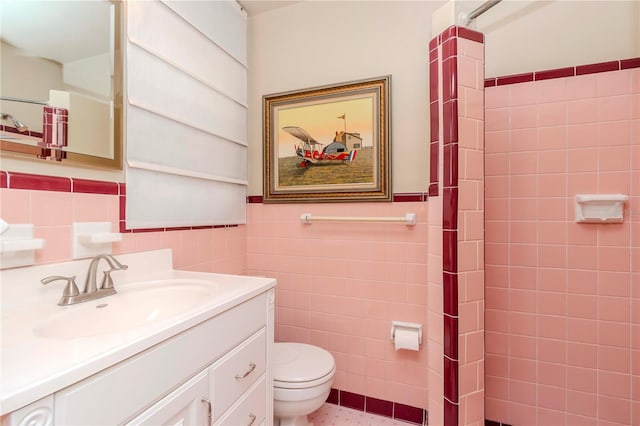 bathroom featuring tiled shower, tile walls, a wainscoted wall, toilet, and vanity