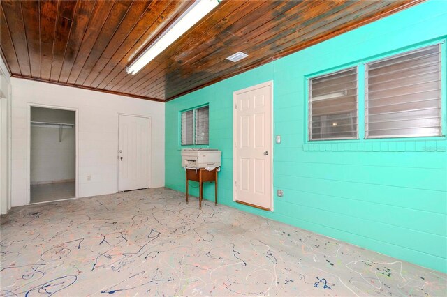 interior space with crown molding, wooden ceiling, unfinished concrete flooring, and two closets
