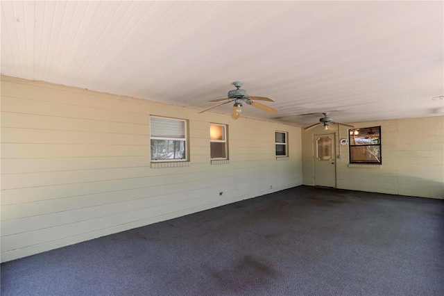 spare room with ceiling fan, a wealth of natural light, and dark colored carpet