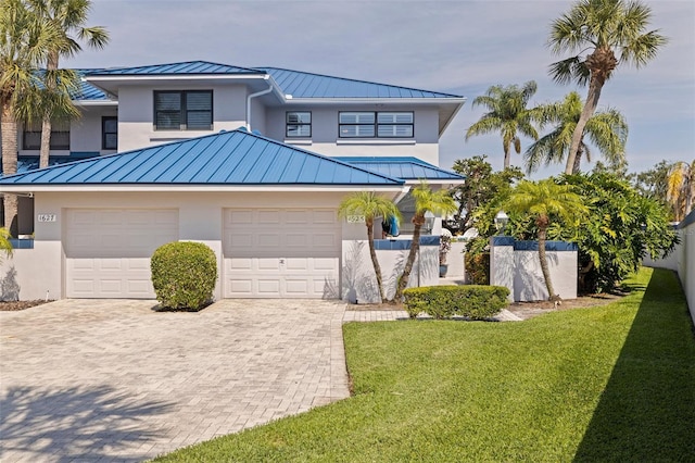 view of front facade with a standing seam roof, metal roof, decorative driveway, stucco siding, and a front lawn