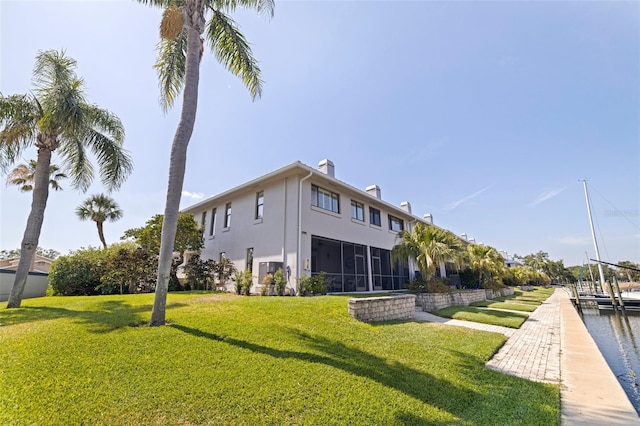 rear view of house featuring a chimney, stucco siding, a sunroom, and a lawn
