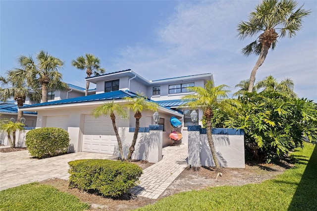 view of front of house with stucco siding, decorative driveway, metal roof, and an attached garage