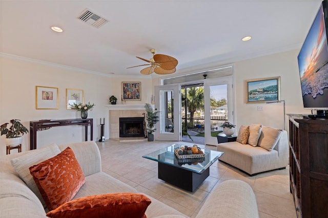 living area with a tiled fireplace, light tile patterned floors, a ceiling fan, visible vents, and ornamental molding