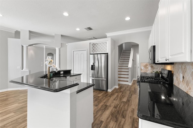 kitchen with a sink, dark countertops, visible vents, stainless steel appliances, and decorative columns