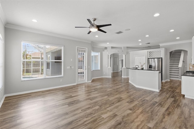 unfurnished living room with visible vents, ceiling fan, crown molding, and arched walkways