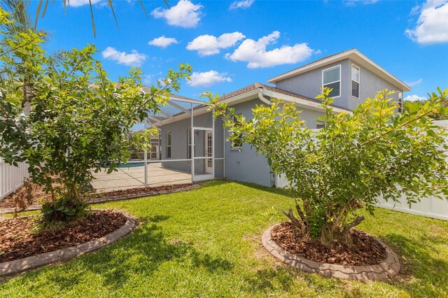 rear view of house featuring a lawn, stucco siding, glass enclosure, and fence