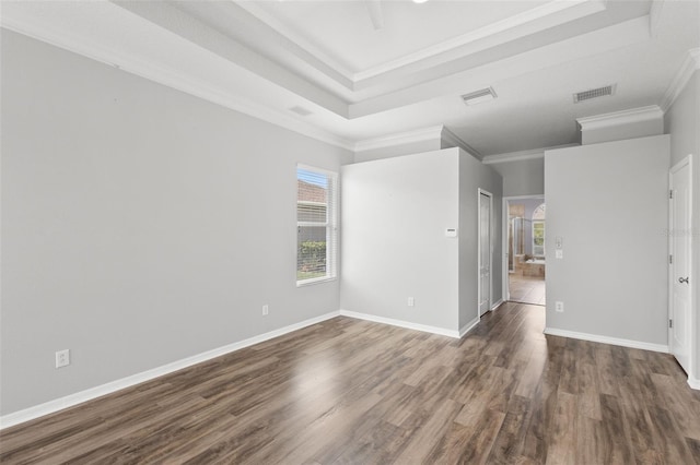 empty room with visible vents, a raised ceiling, ornamental molding, and wood finished floors