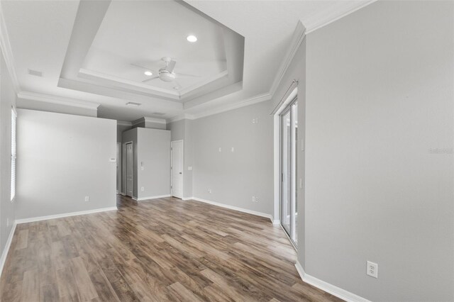 empty room featuring a raised ceiling, a ceiling fan, baseboards, ornamental molding, and wood finished floors