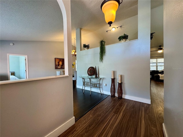 interior space featuring a textured ceiling, wood finished floors, arched walkways, and baseboards