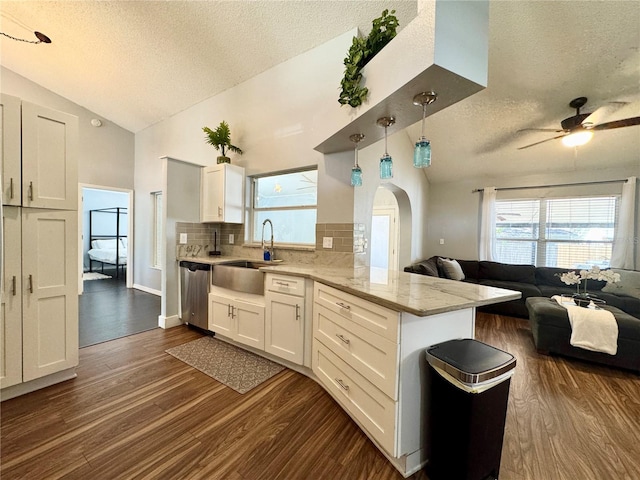 kitchen featuring a textured ceiling, a sink, dishwasher, dark wood finished floors, and a peninsula