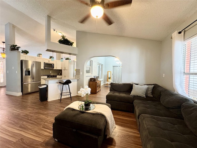 living room with a textured ceiling, ceiling fan, dark wood-style floors, and arched walkways