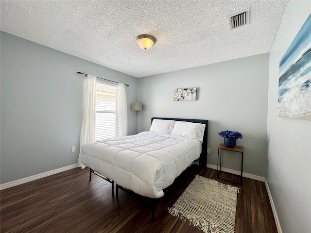 bedroom featuring a textured ceiling, visible vents, wood finished floors, and baseboards