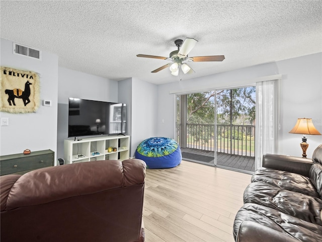 living room with a textured ceiling, ceiling fan, visible vents, and wood finished floors