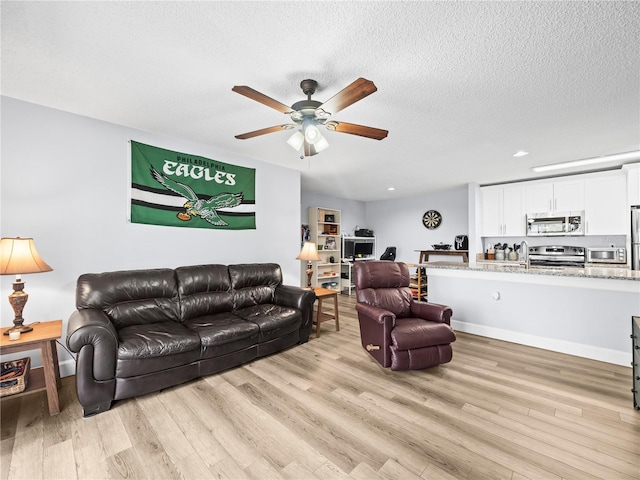 living area with recessed lighting, ceiling fan, light wood-type flooring, and a textured ceiling