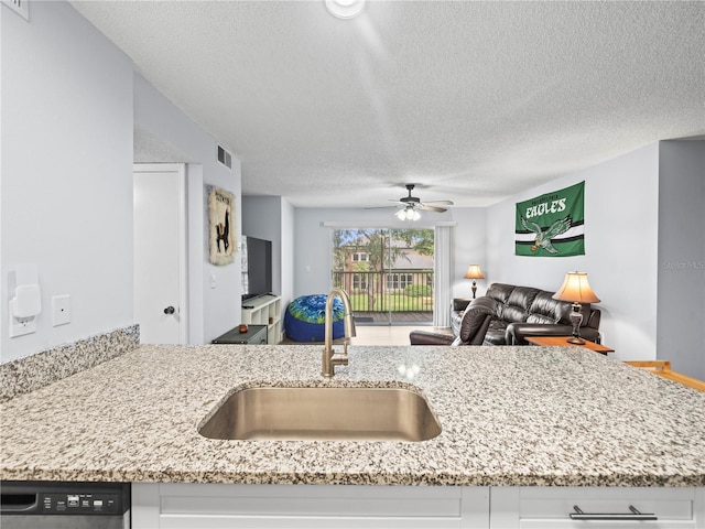 kitchen featuring visible vents, a ceiling fan, a textured ceiling, light stone counters, and a sink