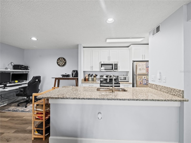 kitchen featuring light stone counters, a sink, a textured ceiling, stainless steel appliances, and white cabinetry