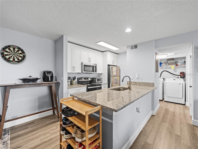 kitchen with a textured ceiling, visible vents, appliances with stainless steel finishes, a sink, and light wood-style flooring