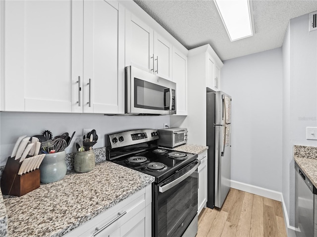 kitchen with baseboards, white cabinets, light stone counters, light wood-style flooring, and stainless steel appliances