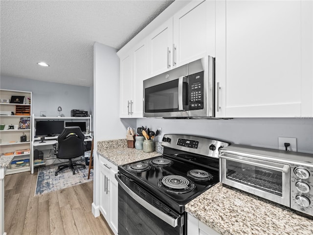 kitchen with light wood-style floors, a textured ceiling, white cabinetry, and appliances with stainless steel finishes