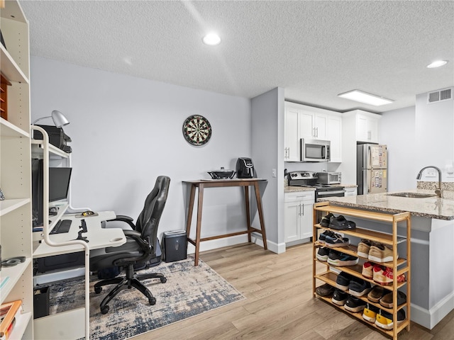 home office featuring a sink, a textured ceiling, light wood-style flooring, recessed lighting, and visible vents