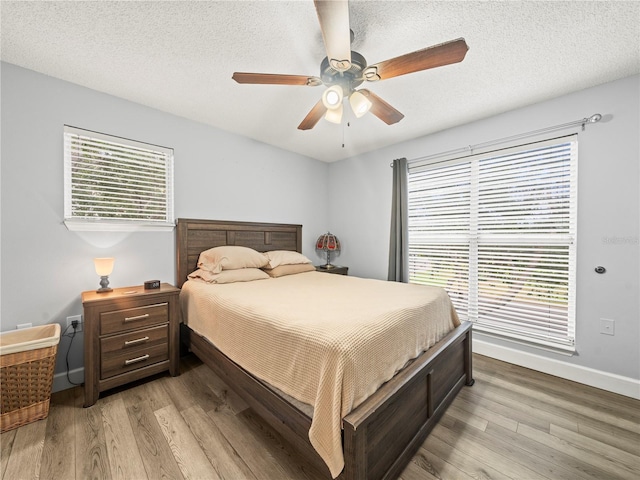 bedroom with baseboards, a ceiling fan, light wood finished floors, and a textured ceiling