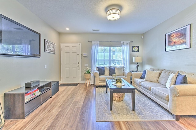 living area with light wood finished floors, a textured ceiling, visible vents, and baseboards