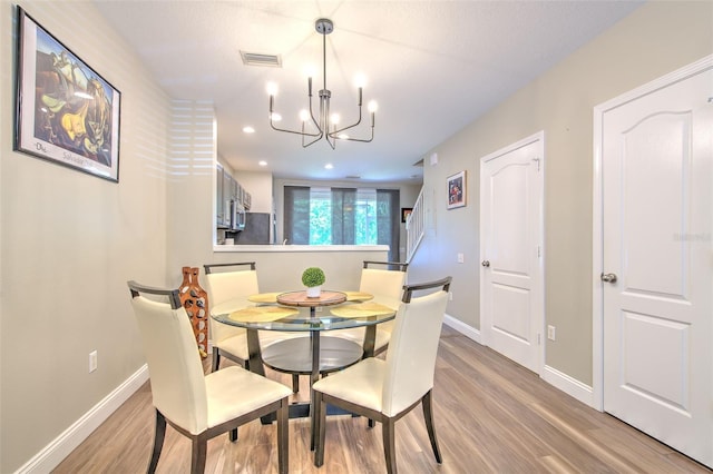 dining space featuring visible vents, light wood-style floors, a chandelier, and baseboards