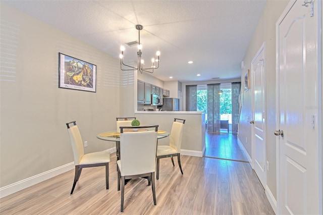 dining room with light wood finished floors, an inviting chandelier, visible vents, and baseboards