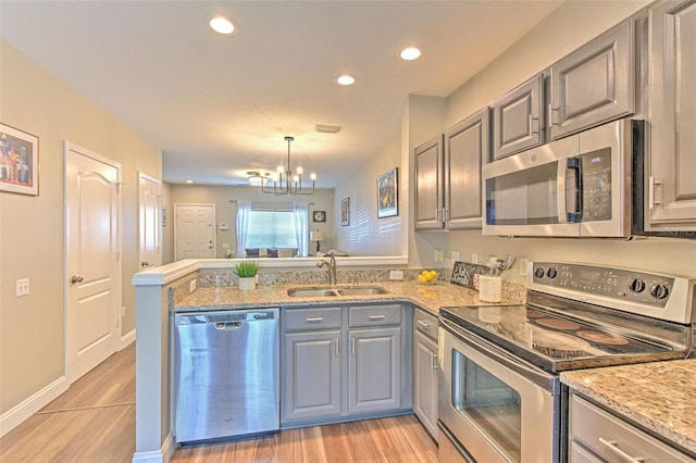 kitchen with a sink, a notable chandelier, a peninsula, gray cabinetry, and appliances with stainless steel finishes
