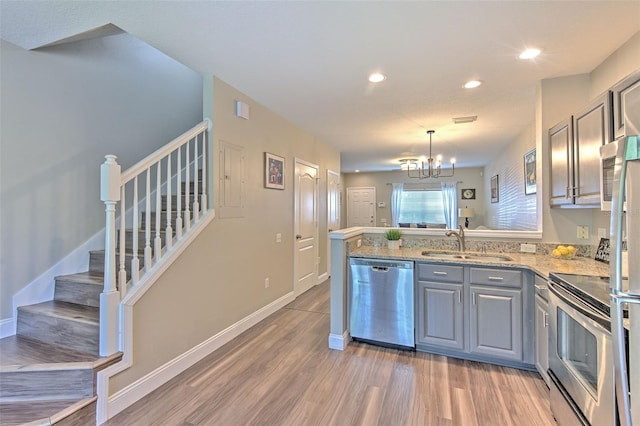kitchen with stainless steel appliances, light wood-style floors, a sink, gray cabinetry, and a peninsula