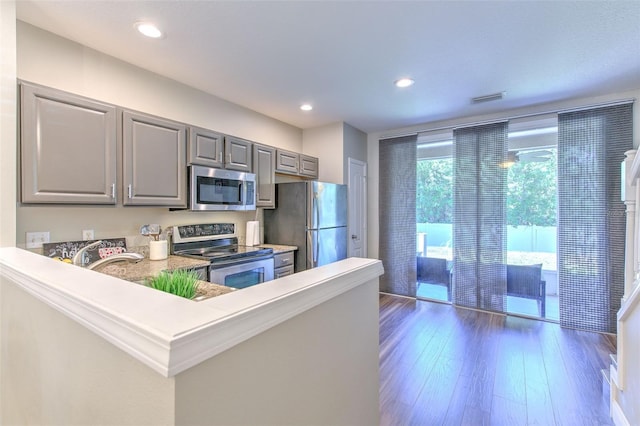 kitchen with recessed lighting, appliances with stainless steel finishes, dark wood-style flooring, gray cabinetry, and a peninsula