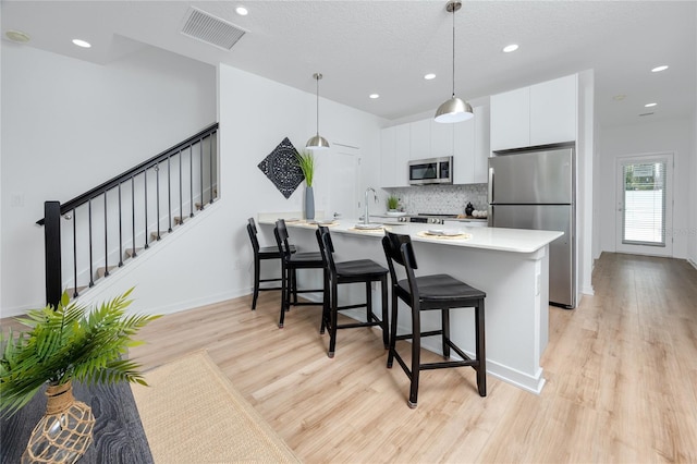 3402 E 28th Ave Unit 6, Tampa, FL 33605 - kitchen featuring stainless steel appliances, light wood-type flooring, a kitchen breakfast bar, tasteful backsplash, and white cabinetry