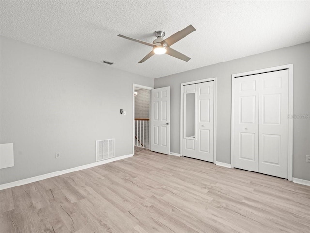 619 2nd St Unit 3, Indian Rocks Beach, FL 33785 - unfurnished bedroom featuring multiple closets, light wood-style flooring, a textured ceiling, baseboards, and a ceiling fan