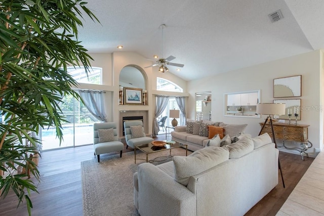 living area featuring visible vents, high vaulted ceiling, wood finished floors, ceiling fan, and a fireplace