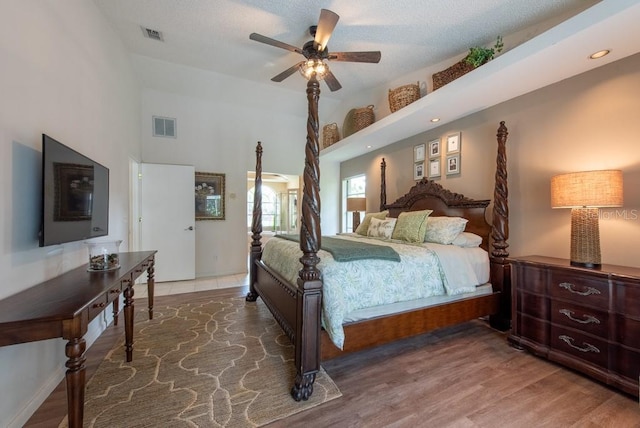 bedroom with ceiling fan, a towering ceiling, wood finished floors, and visible vents