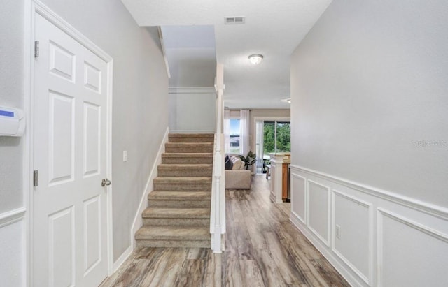stairs featuring visible vents, a wainscoted wall, wood finished floors, and a decorative wall