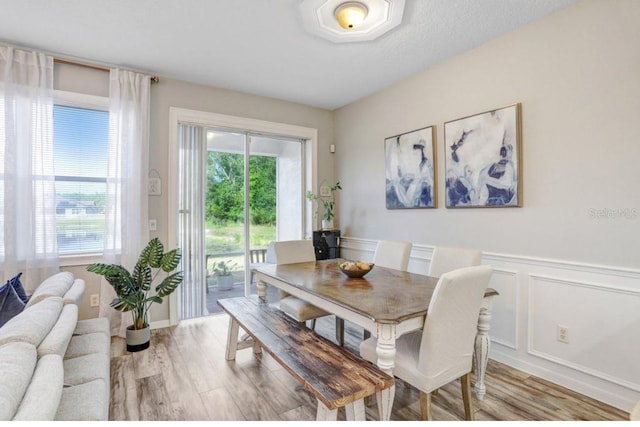 dining area with light wood finished floors, wainscoting, and a decorative wall