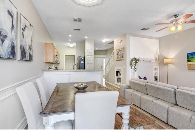 dining room featuring wood finished floors, a ceiling fan, visible vents, and stairway